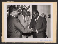 8x10 Black and White mounted on 8 1/2x11 1/4 piece of cardboard. On back the label reads, &quot;M. Alphonse Boni, President of the Ivorian Supreme Court (right) greets Dean Clyde Ferguson of Howard Law School, Washington D.C., as Wilbert C. Petty, Director of American Cultural Center looks on.&quot; Ca. Early 1960s. Front (bottom right) is signed, &quot; T.H. [unreadable] - Howard.&quot; Digital Object