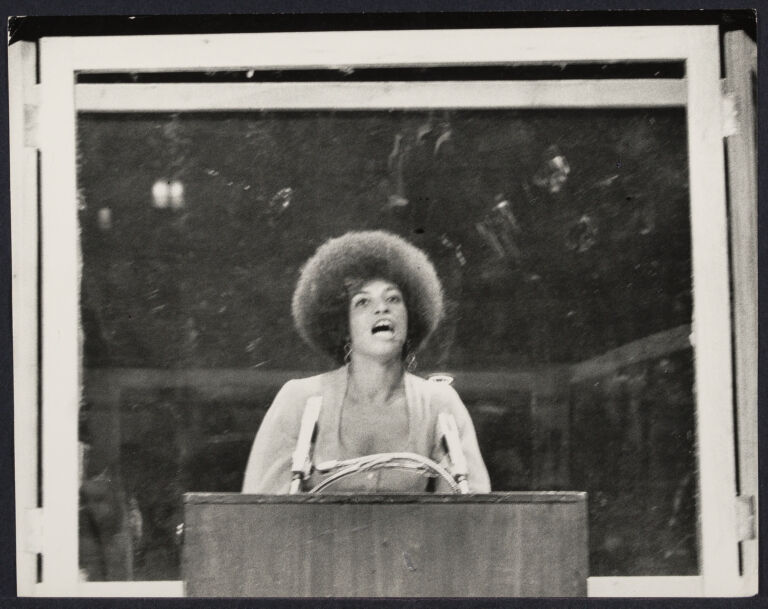 Angela Davis, behind bullet-proof glass, as she performs