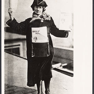 Print of a black and white photograph of a woman wearing a dark coat with a fur collar holding flyers in each hand and wearing a bag with flyers inside