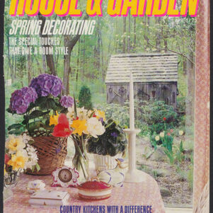 Cover of the magazine House & Garden with a full-color photograph of a decorated table in front of a window through which is a wooden shack in a forest