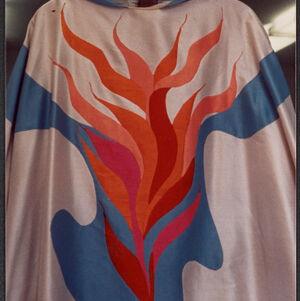 Color photograph of a poncho decorated with a red and blue flame-like design on white