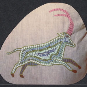 Needlework of a horned animal in blue, white, and pink on a light pink ground