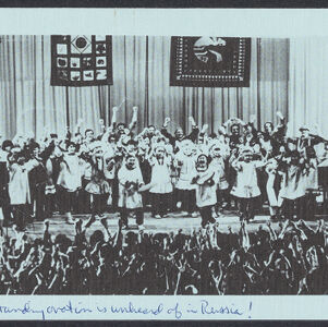 Printed reproduction of a black and white photograph on light blue paper of a group of performers celebrating on a stage in front of a standing ovation with handwritten annotation