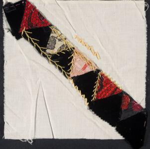 Strip of quilted fabric with black and red patterned triangles overlaid with gold embroidery thread and attached diagonally to a white piece of fabric