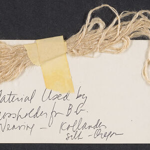 Sample of beige yarn attached with tape to a white card with handwritten annotations in black ink