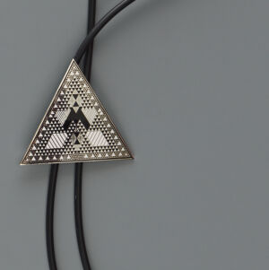 Bolo tie with an upward pointing triangular clasp filled with geometric designs in shiny silver and a black tie