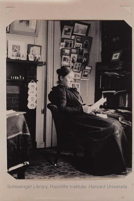 Marie Gallison seated in a chair in a study, reading a book in a long dark dress.