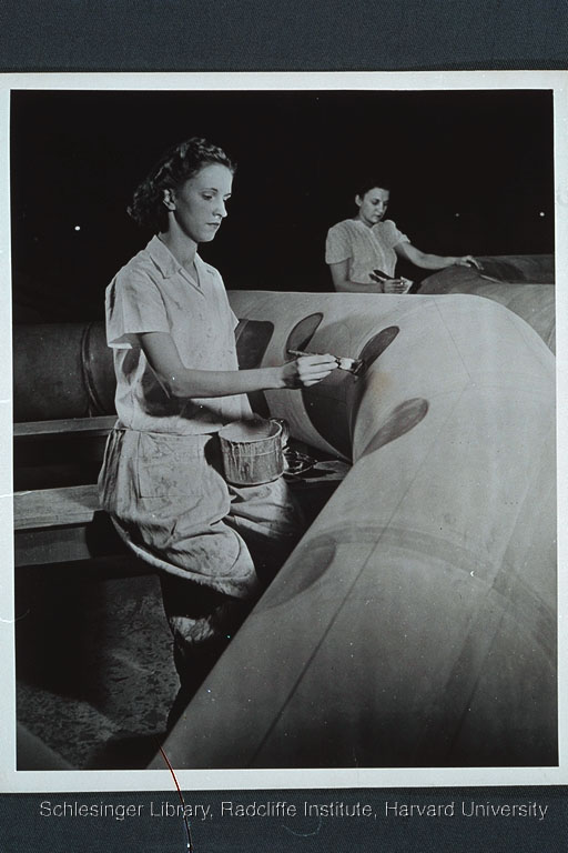 Two women applying a coat of rubber cement to the exterior of an assault boat