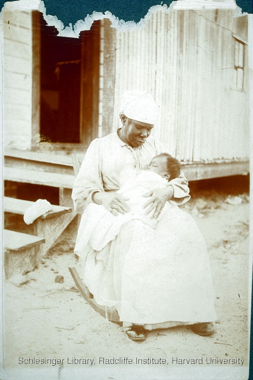 unidentified african american woman holdinger her baby in her lap, in front of her house.
