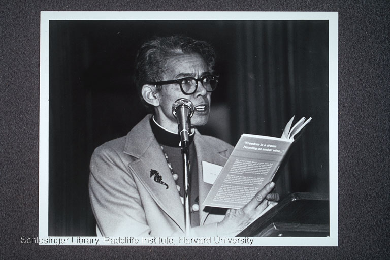 Pauli Murray at a microphone, reading her poetry, 1977.