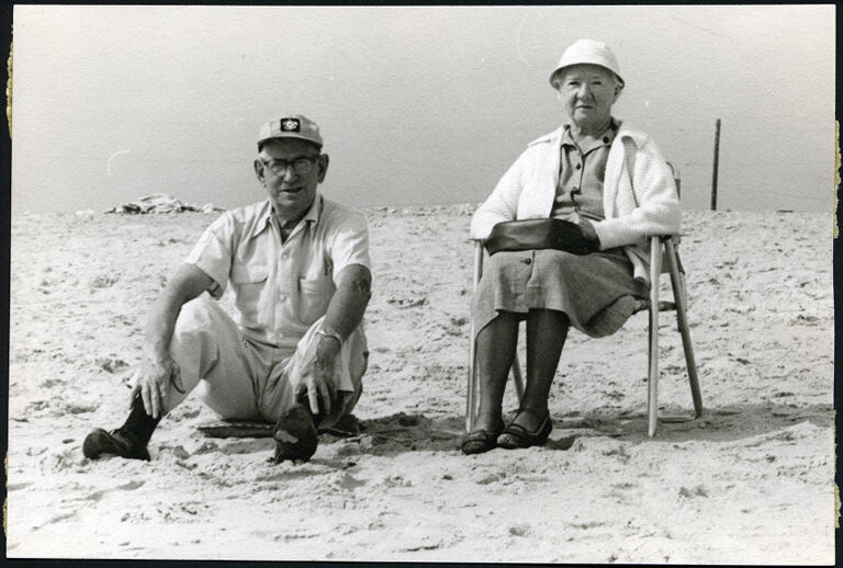 elderly white couple seated next to one another on the beach.