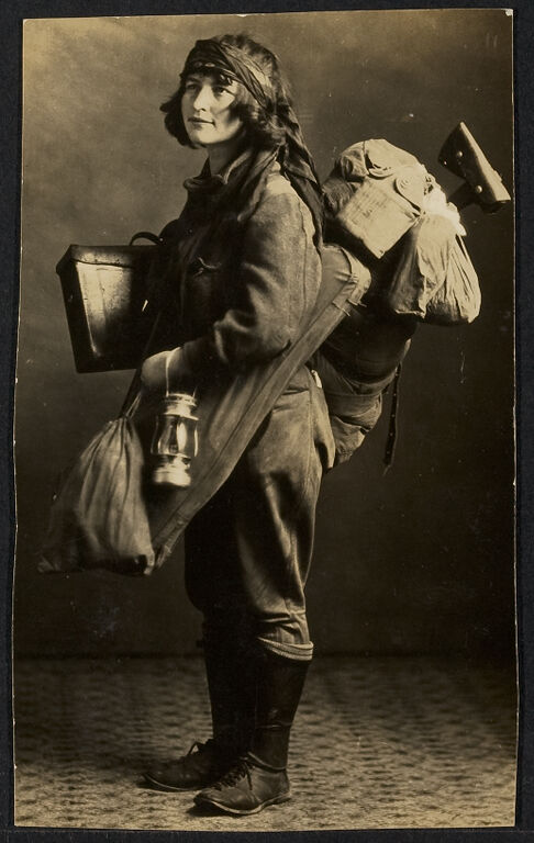 Woman outfitted with camping gear, including and axe and a lantern