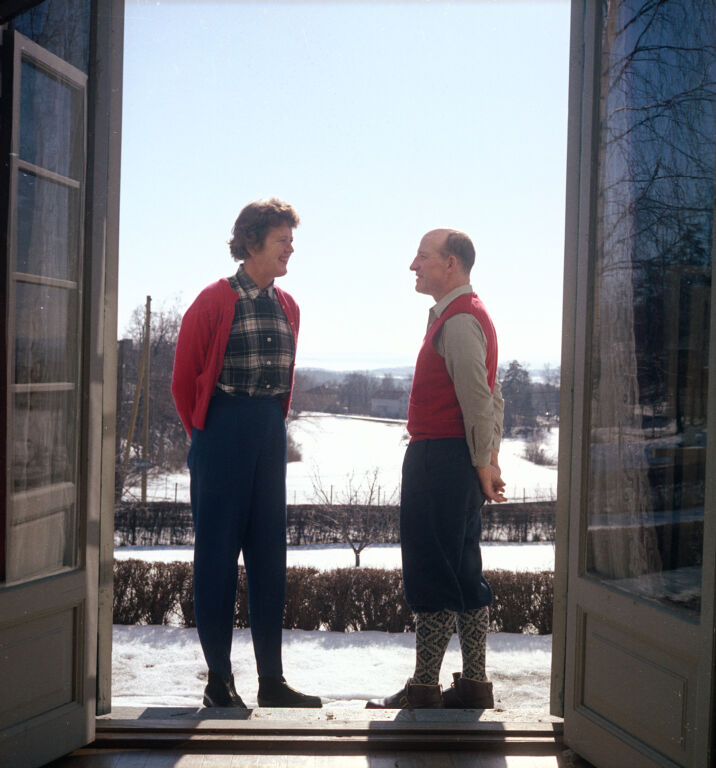 Paul and Julia Child face one another, arms tucked behind their backs, in front of a winter scene in Oslo; prepared for Valentines that year; in color