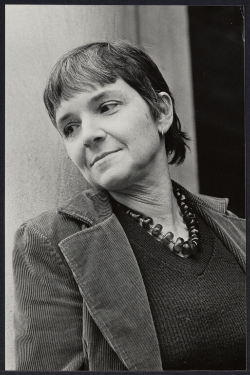 Portrait of Adrienne Rich wearing a corduroy jacket, looking off camera, in black and white. 