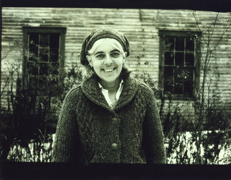 Cora Brooks standing outside a building in winter wearing a matching cardigan and hat, smiling.