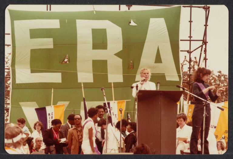 Woman speaking at a podium in front of large ERA banner.